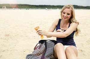 Junge Frau cremt sich am Strand mit Sonnencreme ein.