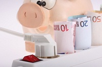 Ein Sparschwein hinter einer Steckdose, in der Euro-Geldscheine stecken.