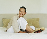 Frau liest Buch in Hotelbett