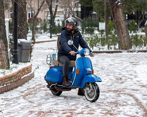 Ein Mann fährt auf einem blauen Roller durch den Schnee.