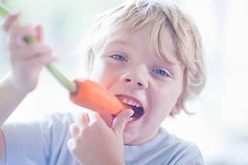 Ein kleiner, blonder Junge isst eine Karotte.