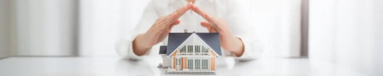 Hände halten schützend ein Miniaturhaus