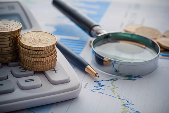 Ein Taschenrechner mit einem Stapel Münzen darauf und einer Lupe an der Seite