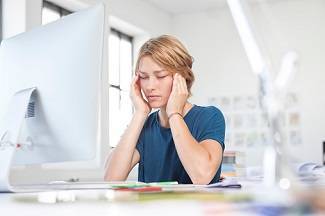 Frau mit Kopfschmerzen vor Bildschirm im Büro