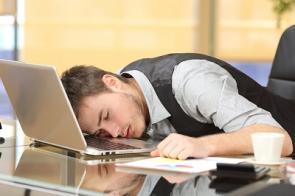 Angestellter schläft im Büro vor dem Laptop