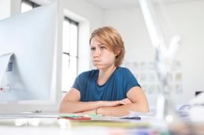 Junge Frau sitzt gestresst am Arbeitsplatz
