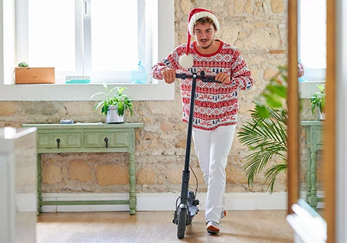 Ein Mann in weihnachtlichem Outfit schiebt einen E-Scooter druch seine Wohnung.