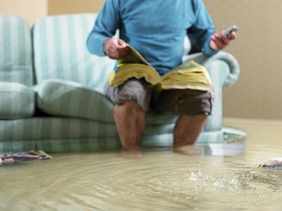 Ein Mann sitzt telefonierend auf der Couch und ist umgeben von Hochwasser.
