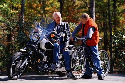 Älterer Mann sitzt auf einem Motorrad. Daneben steht ein Junge mit seinem Fahrrad.
