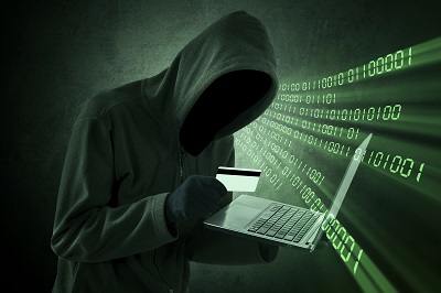 Verhüllte Person steht vor einem PC und suggeriert ein Cyberverbrechen.