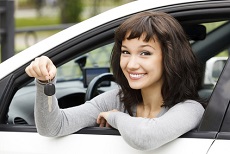 Junge Frau sitzt am Fahrersitz und hält den Autoschlüssel aus dem Fenster