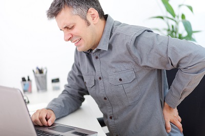 Angestellter mit Rückenschmerzen am Schreibtisch