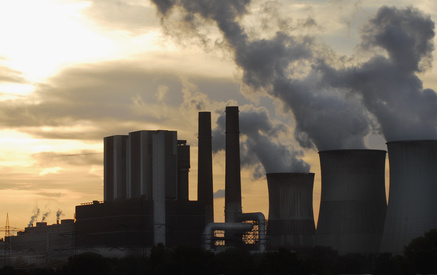 Silhouette eines Kohlekraftwerks mit aufsteigendem Rauch vor einem Sonnenuntergang