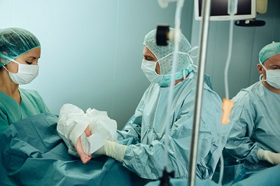 Arzt übergibt OP-Schwester ein Neugeborenes nach einem Kaiserschnitt.