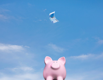 Ein 20 Euro Schein fliegt auf ein Sparschwein. Foto: Gettyimages/Deborah Harrison