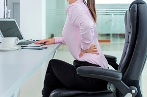 Angestellte mit Rückenschmerzen sitzt am Schreibtisch