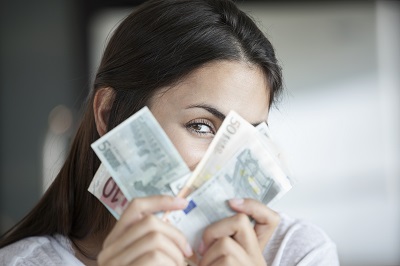 Schufa und Bonität beim Kredit: Brünette Frau blickt durch Euro-Geldscheine