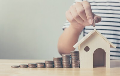 Anschlussfinanzierung Immobilie Person wirft Münze in Haus