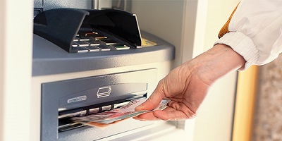 Person hebt Bargeld an Geldautomat in Euro Banknoten ab.