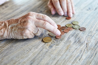 Ältere Frau zählt Münzen auf einem Tisch.
