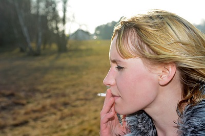 Junge Frau raucht draußen in der Landschaft.