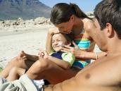 Mutter cremt Kind am Strand mit Sonnencreme ein