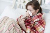 Eine Frau liegt krank im Bett und überprüft ihre Temperatur.