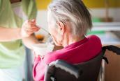 Pflegerin hilft Seniorin im Rollstuhl beim Essen.