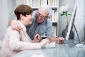 Älteres Paar sitzt vor einem Rechner mit Kreditkarte.