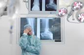 Ein gestresster Chirurg steht vor einer Wand mit Röntgenbildern.