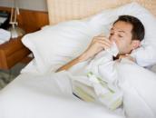 Ein Mann liegt krank im Bett und schnäuzt in ein Taschentuch.