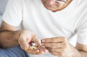 Älterer Mann hält mehrere Tabletten in der Hand.