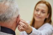 Ärztin setzt einem älteren Patienten ein Hörgerät ein.