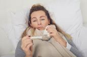 Frau liegt krank im Bett mit Fieberthermometer
