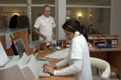 Arzthelferin an der Rezeption mit Arzt im Hintergrund