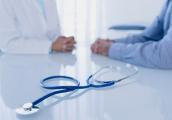 Ärztin und Patientin sitzen an einem Tisch - Stethoskop im Vordergrund