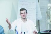 Junger Arzt sitzt im Büro mit Flipchart und Skelett im Hintergrund