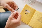 Hand hält Impfdosis mit Impfpass im Hintergrund