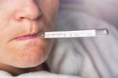 Frau misst Temperatur mit Thermometer im Mund