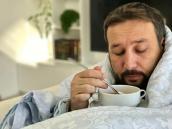 Ein in eine Decke eingewickelter Mann trinkt Suppe.