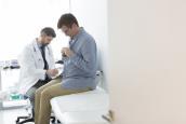Patient sitzt im Behandlungszimmer beim Arzt auf der Liege.