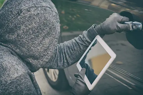 Ein Dieb im Kapuzenpulli stiehlt ein Tablet aus einem Auto.