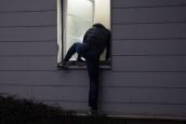 Ein Einbrecher steigt nachts durch das Fenster eines Hauses in eine Wohnung ein.
