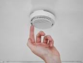 Eine Hand greift nach einem Rauchmelder, der an der Decke montiert ist.