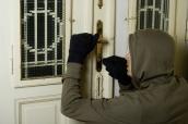 Ein Einbrecher versucht eine eine Wohnungstür aufzubrechen.
