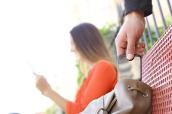 Während eine Frau auf einer Bank sitzt und abgelenkt ist, stiehlt ein Dieb ihr Handy aus ihrer Tasche.