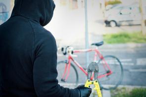 Ein dunkel gekleideter Dieb steht mit einer Zange in der Hand vor einem Fahrrad.