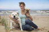 Eine Fraus sitzt am Strand und umarmt eine Bulldogge und einen Yorkshire-Terrier.