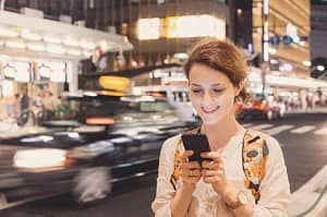 Touristin mit Smartphone abends an einer Straße in Tokio