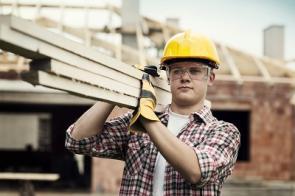 Bauarbeiter mit Helm trägt Holzlatten